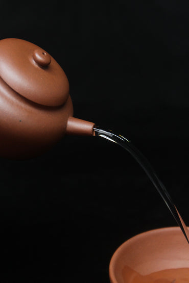 Pour of a vintage small Yixing teapot made of dicaoqing purple clay.