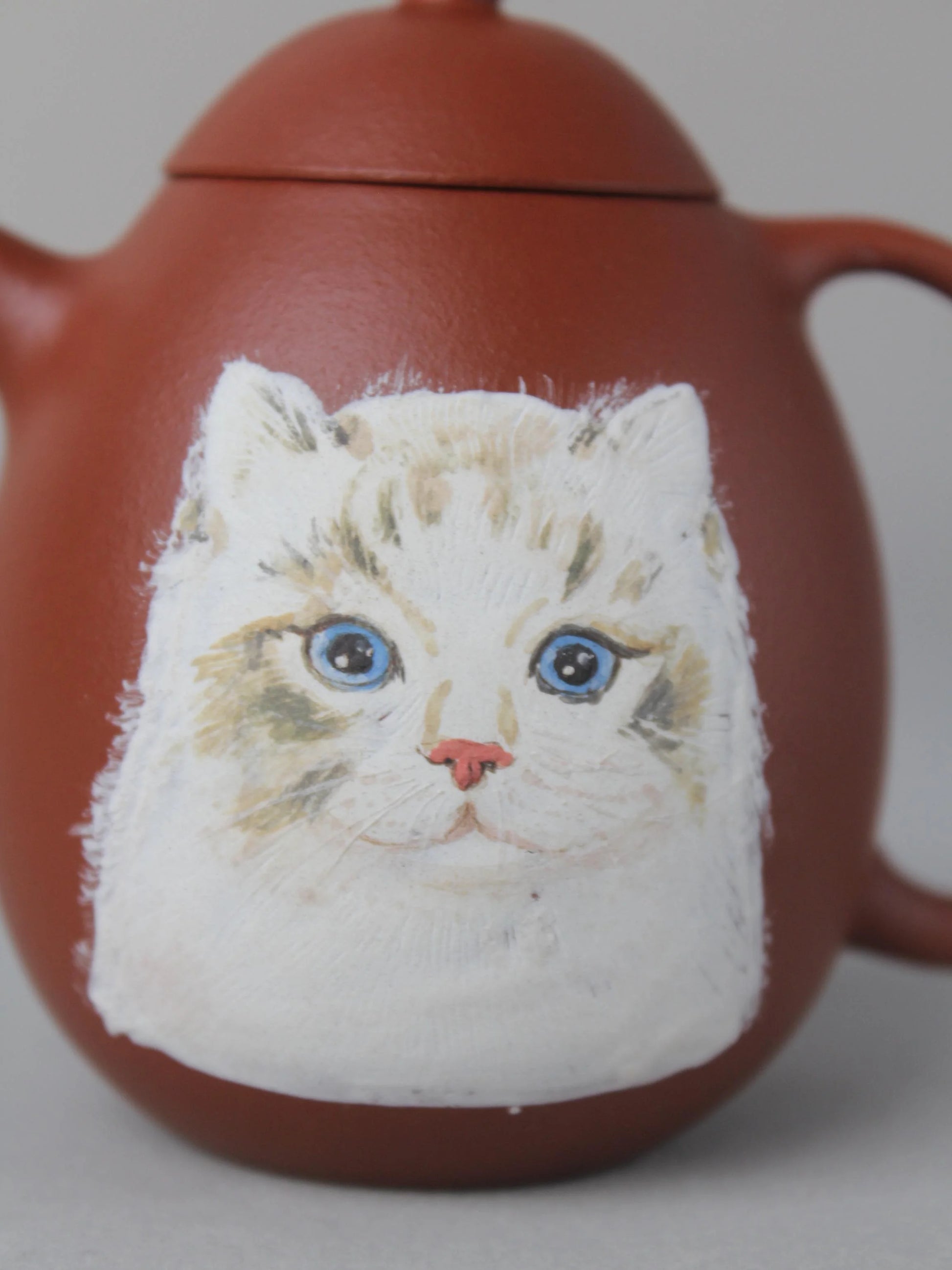 This dragon egg teapot has a painting of a cat on it.